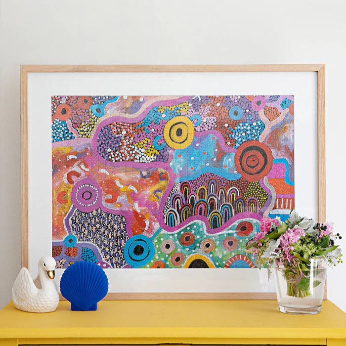 Colorful abstract artwork in a wooden frame on a yellow surface with decorative items.